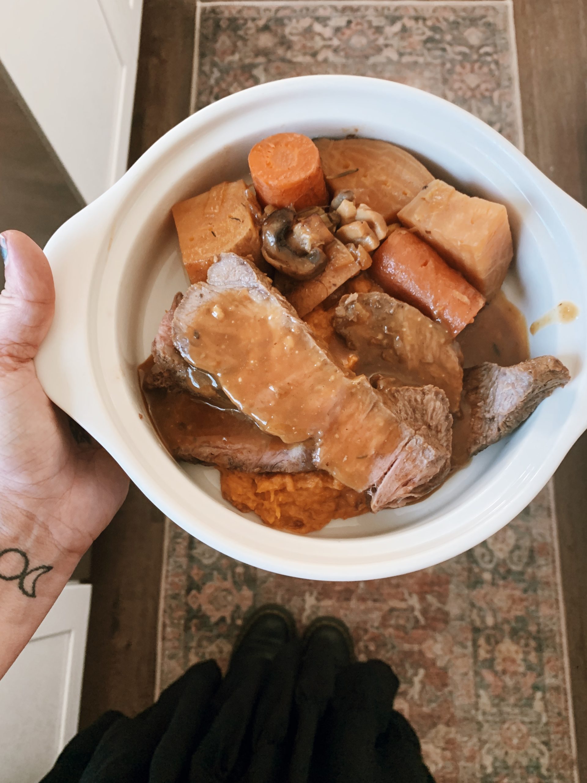 iPhone photo of sliced beef chuck blade roast over sweet potato mash and roasted golden veggies with a goddess tattoo on the wrist