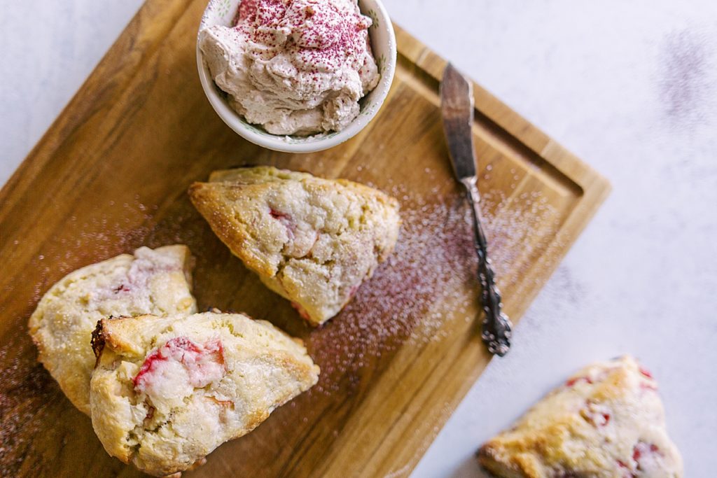 Strawberry rhubarb scones with clotted cream and rose, perfect for afternoon tea, served on a wooden cutting board and tea knife.